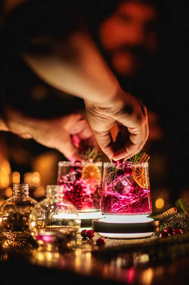 A hand garnishing a festive cocktail with orange and rosemary